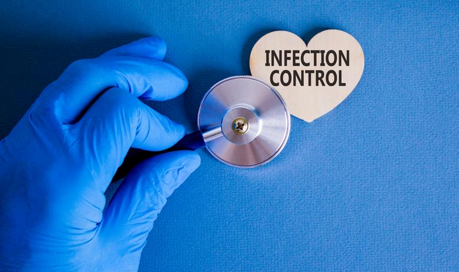 Gloved hand holding a stethoscope next to a wooden heart that reads Infection Control